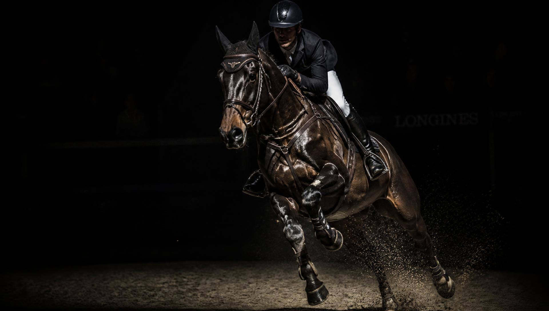 Show jumping horse and rider galloping under a spotlight